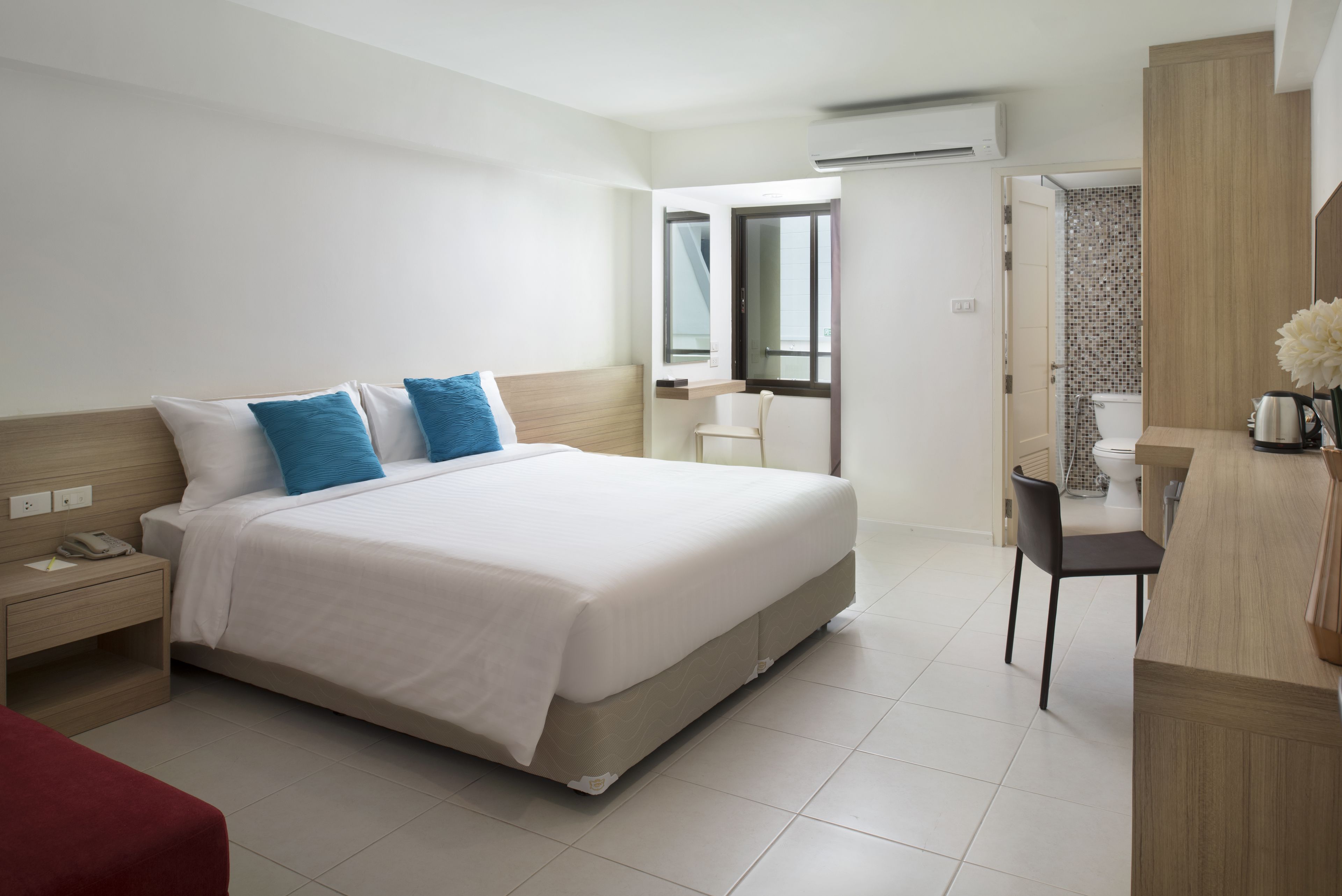 A modern hotel room with a large bed, bedside table, and a desk with a chair.