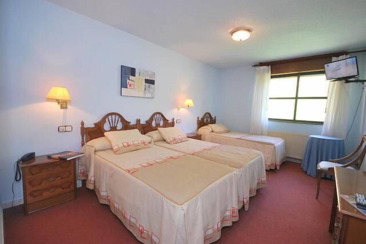 Une chambre d’hôtel avec deux lits, un bureau, une chaise, une télévision et une fenêtre avec des rideaux.
