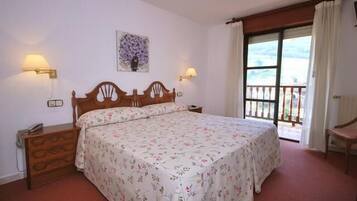 A bedroom with a wooden bed, floral bedspread, two bedside lamps, a nightstand, and a window with curtains.