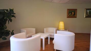 Habitación con muebles blancos, incluyendo sillas, una mesa, una lámpara y dos cuadros en la pared.