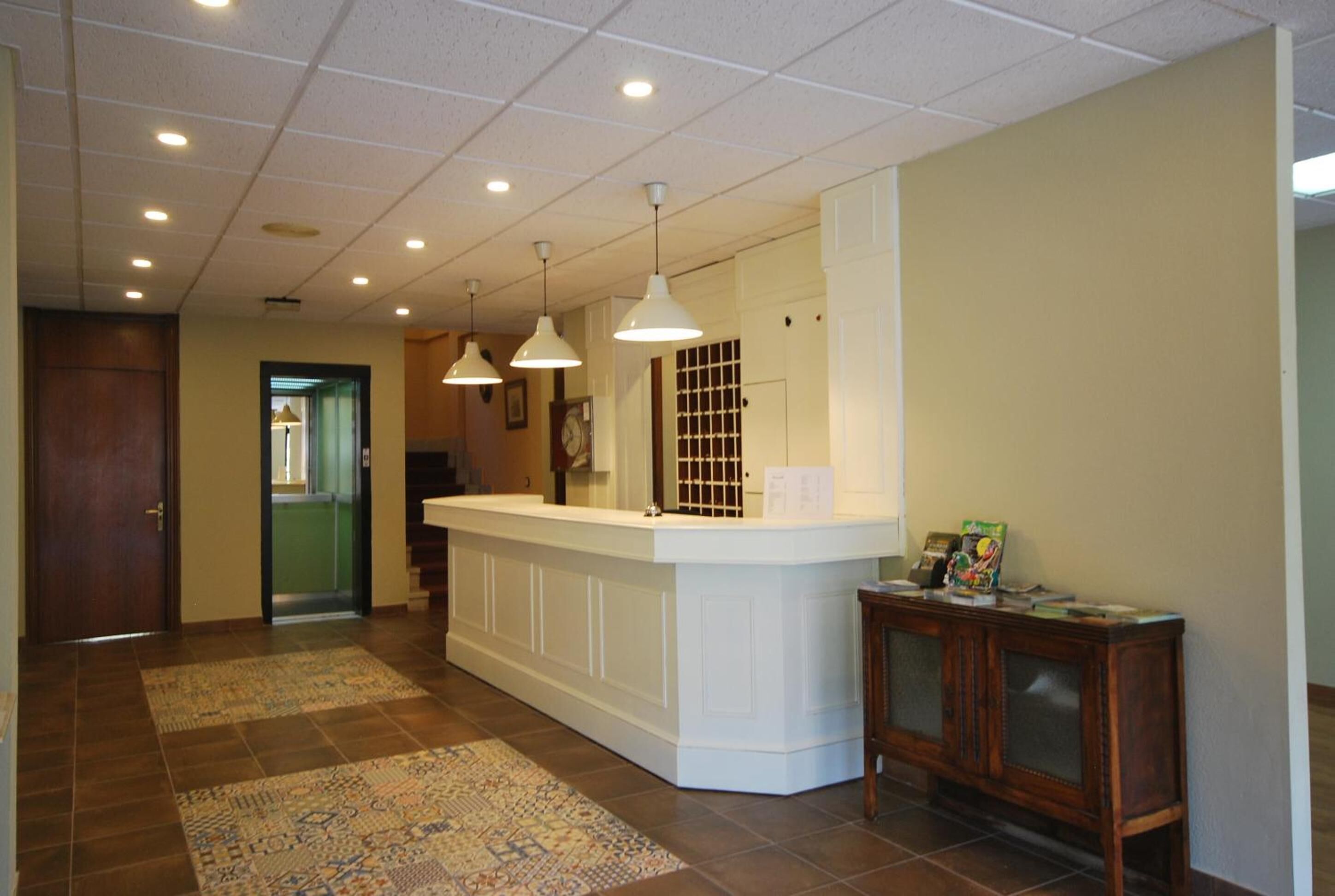 A reception area with a white counter, pendant lighting, a patterned rug, and a wooden side table with a clock.