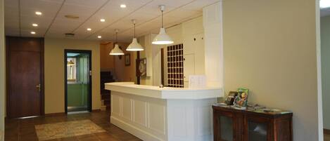 A reception area with a white counter, pendant lighting, a patterned rug, and a wooden side table with a clock.