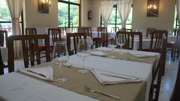 Un comedor con mesas preparadas para dos, cada una con mantel blanco, cubiertos y copas de vino.