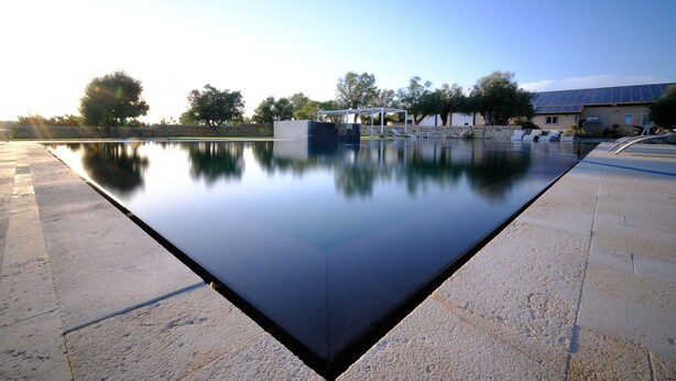 A rectangular pool with a clear reflection, surrounded by a stone walkway and trees. - La Mela di Venere (Palazzolo Acreide)