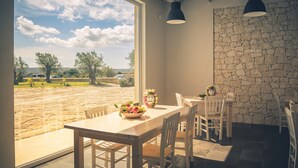 A dining area with a table and chairs, a stone wall, and a view of a landscape with trees and a vehicle. - La Mela di Venere (Palazzolo Acreide)