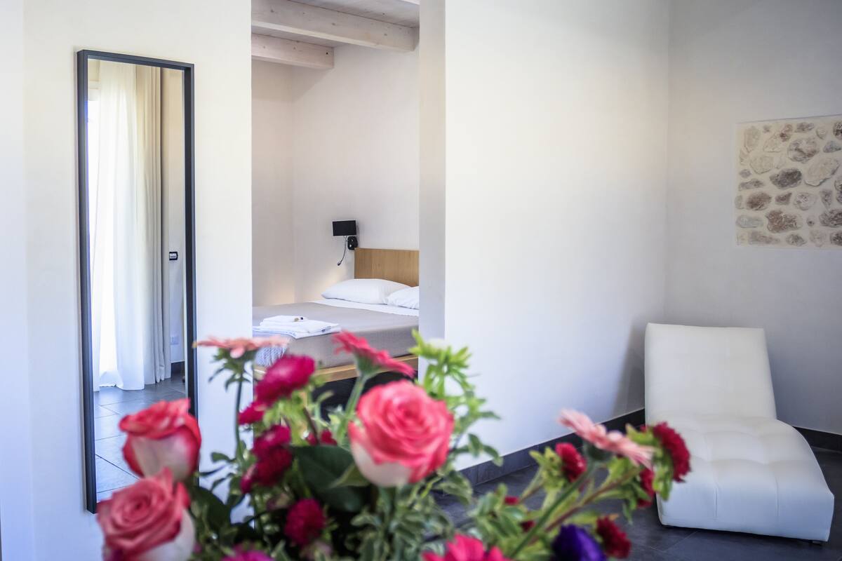 Una habitación de hotel moderna con una cama, un sillón blanco y un espejo grande.