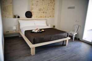 A modern bedroom with a large bed, a bedside table with a lamp, a chair, and a tray with breakfast items. - La Mela di Venere (Palazzolo Acreide)