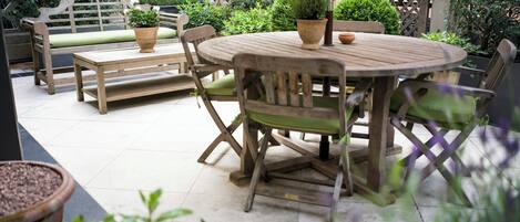 Eine Terrasse mit einem runden Holztisch, zwei Holzbanken und Topfpflanzen.
