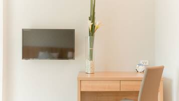 Un espacio de oficina minimalista con un escritorio de madera, un televisor montado en la pared y un jarrón con flores.