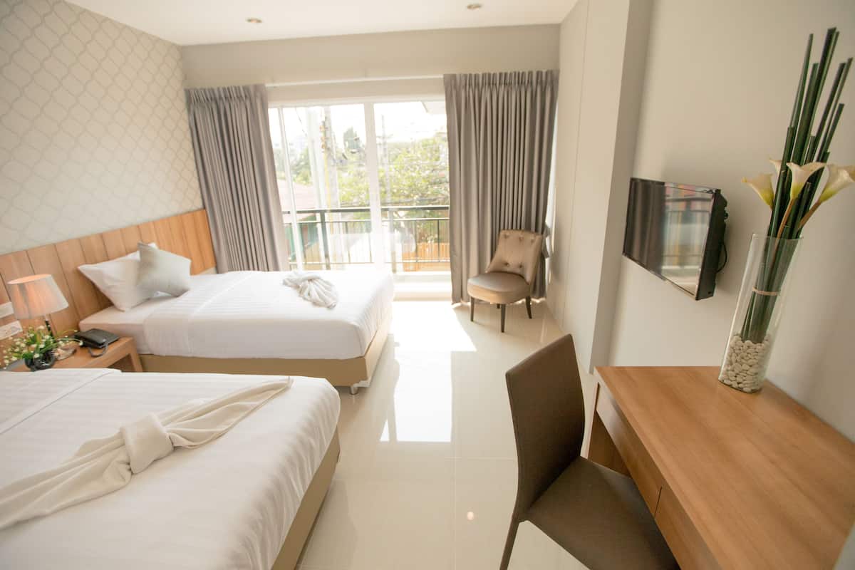 Ein Hotelzimmer mit zwei Betten, einem Holztisch, einem Stuhl, einem Fernseher und einem großen Fenster mit Vorhängen.