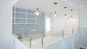 Ein modernes Badezimmer mit einer gläsernen Waschtischablage, einer Fliesenrückwand und Pendelleuchten.