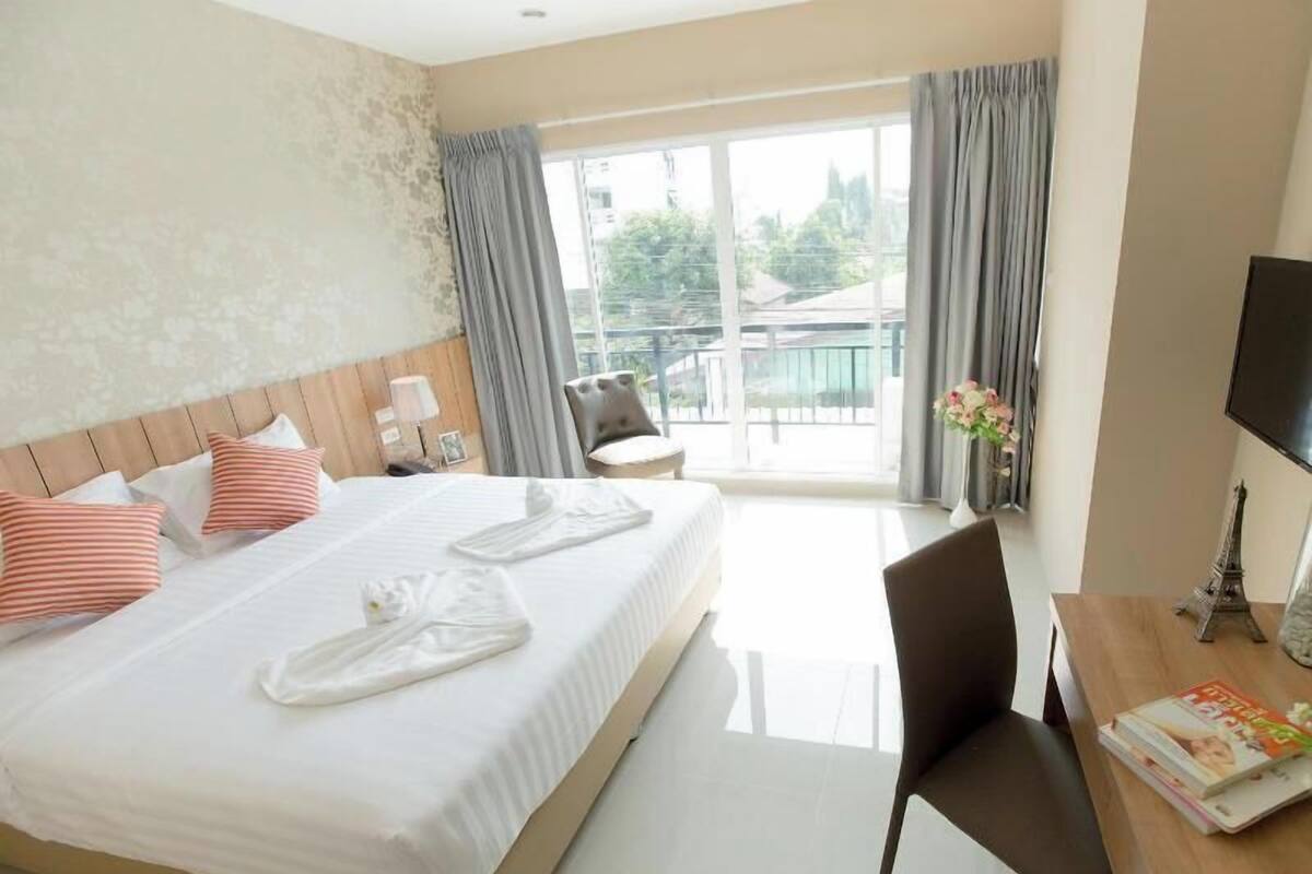Ein Hotelzimmer mit einem großen Bett, einem Schreibtisch, einem Sessel, einem Fernseher und einem Balkon mit Vorhängen.