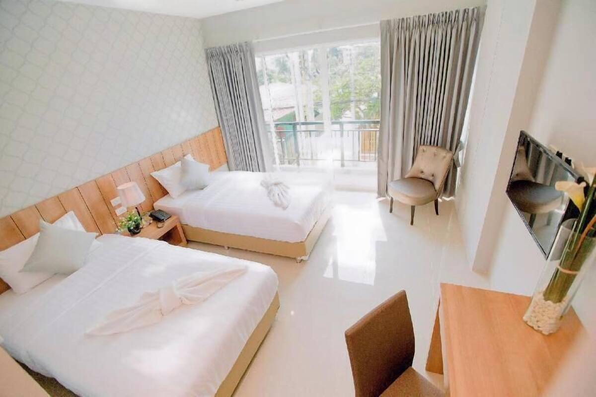 Ein Hotelzimmer mit zwei Betten, einem Balkon, einem Sessel, einem Schreibtisch und einem Fernseher.
