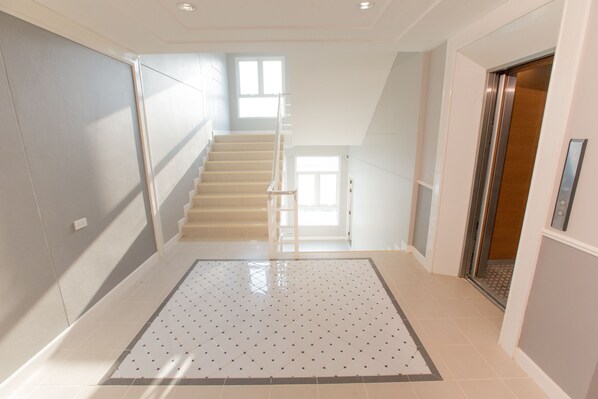 A modern interior with a staircase leading to an upper floor, a tiled floor, and a door with an elevator.