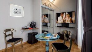 A compact living space with a coffee station, a television, and a small table with a magazine. - QT Suites Roma (Rome)