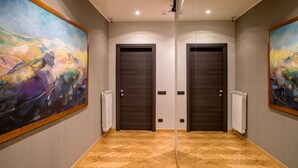 A hallway with two dark wooden doors, a radiator, and a large abstract painting on the left wall. - QT Suites Roma (Rome)