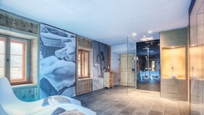 A modern spa room with a large mural, a massage chair, and a shower area.