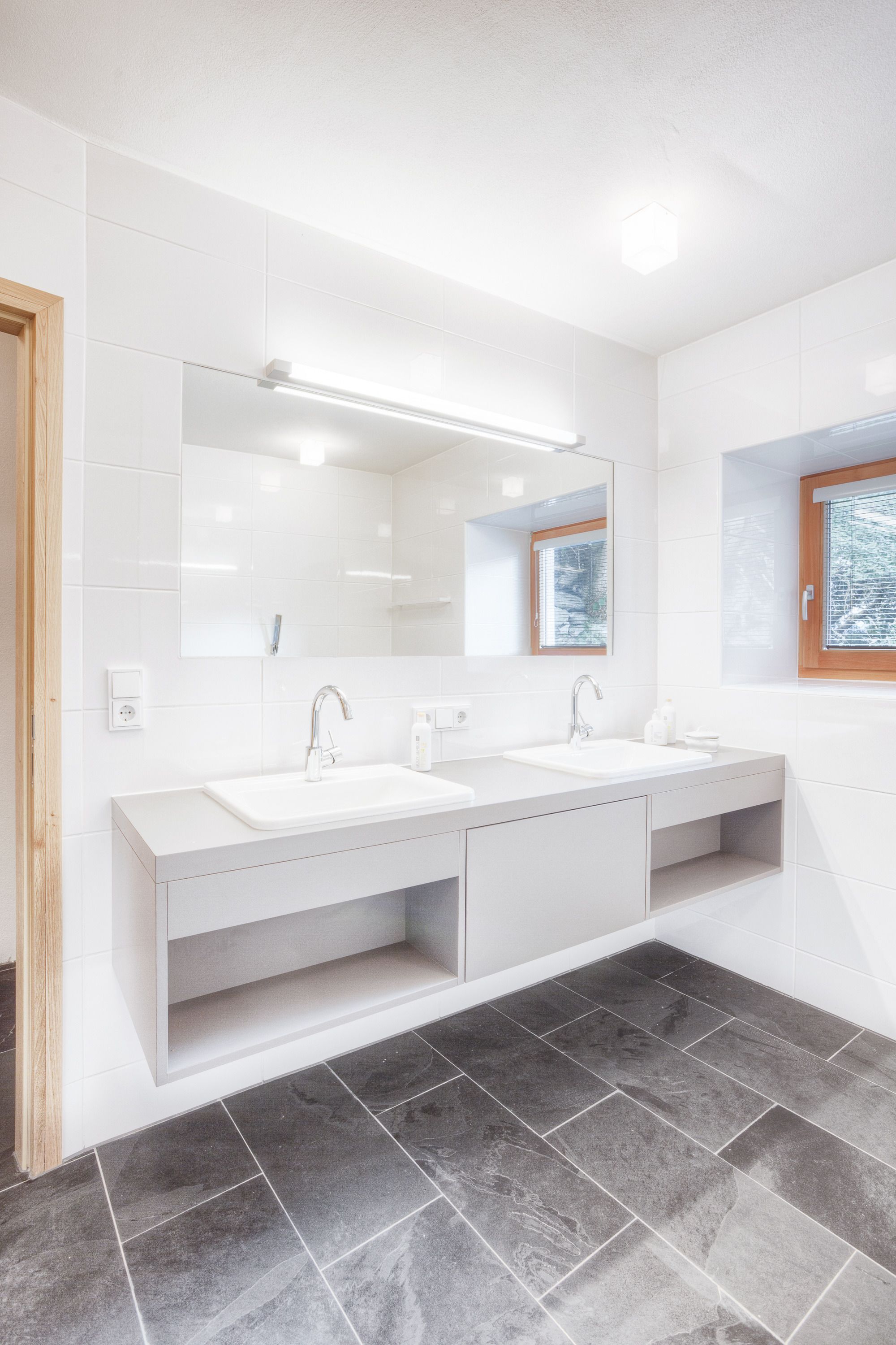 Ein modernes Badezimmer mit zwei Waschbecken, einem großen Spiegel und einem Fenster mit Aussicht.