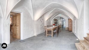 A spacious hallway with a high ceiling and arched design, leading to a dining area with a wooden table and chairs.