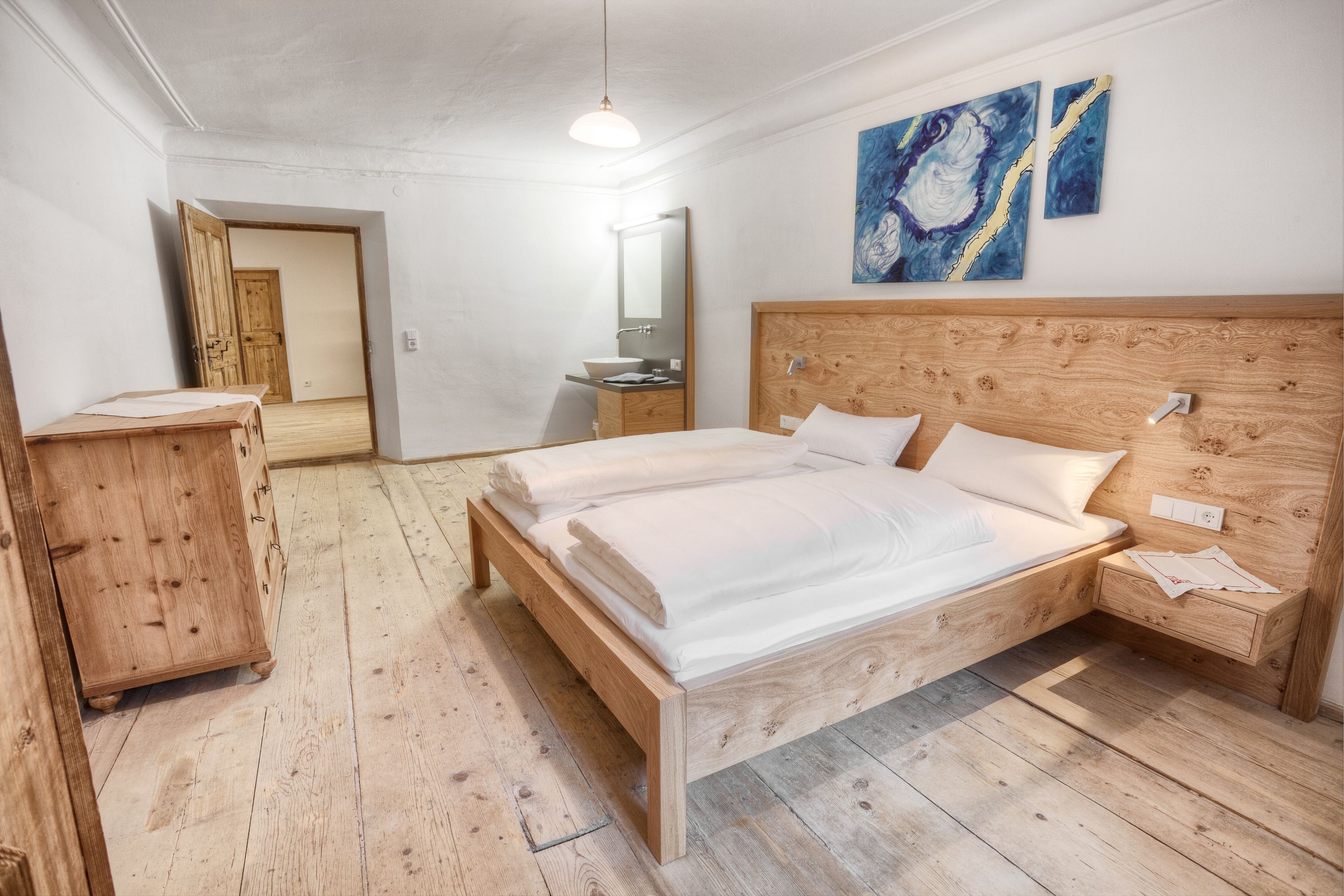 Un dormitorio con una cama de madera, una mesita de noche, un aparador de madera, un espejo y arte abstracto en la pared.