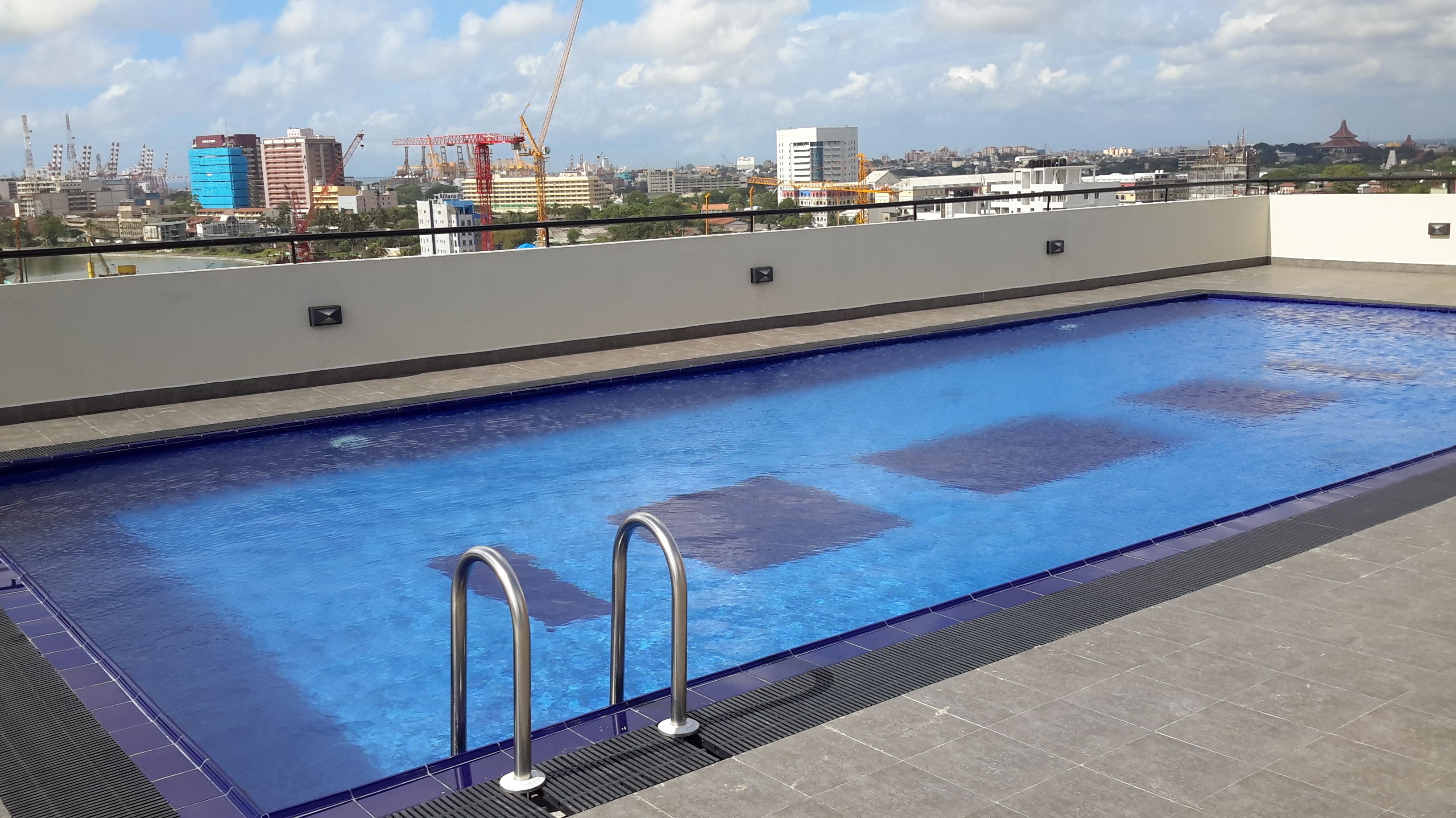 A rooftop swimming pool with a cityscape view, including buildings and cranes.