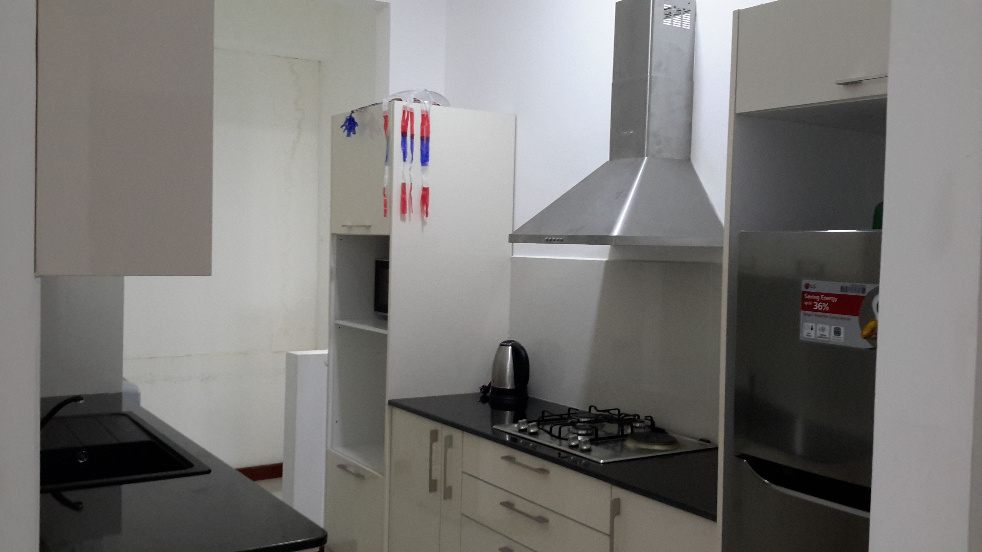 A compact kitchen with a gas stove, a stainless steel range hood, and a refrigerator.