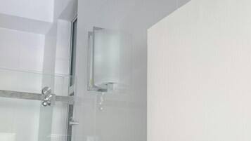Un baño moderno con cabina de ducha de vidrio, un cabezal de ducha visible y un panel de control en la pared.