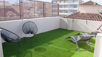 Een terras op het dak met kunstgras, twee zwarte frame stoelen en twee grijze loungestoelen.
