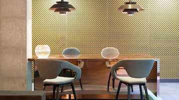 Een modern interieur met een behang met patroon, twee hanglampen en twee stoelen bij een glazen tafel.