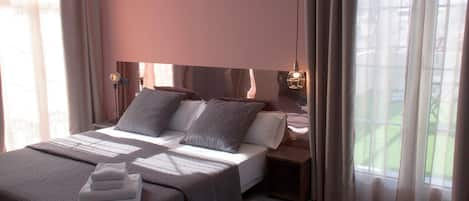Una habitación de hotel moderna con una cama grande, dos mesitas de noche y vistas al exterior.