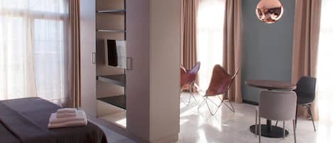 Quarto de hotel moderno com cama, guarda-roupa embutido, área de estar com cadeiras e uma mesa redonda.