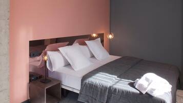 Un lit bien fait, avec une literie blanche et grise, une table de chevet avec une lampe et un luminaire fixé au mur.