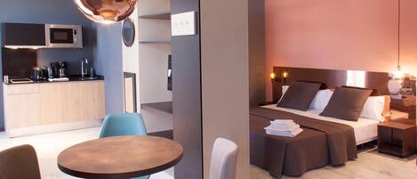 Una habitación de hotel moderna con cama, mesitas de noche, escritorio y kitchenette.