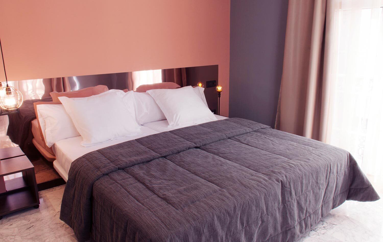 A neatly made bed with white and gray linens, a dark gray bedspread, and a wooden headboard.