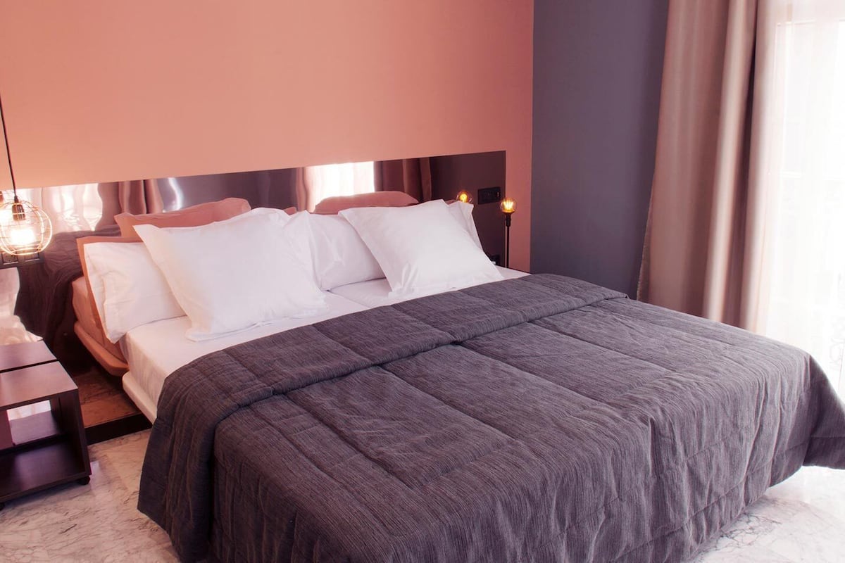 A neatly made bed with white and gray linens, a dark gray bedspread, and a wooden headboard.