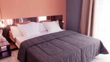 A neatly made bed with a dark grey bedspread and white pillows, a bedside table with a lamp, and a window with curtains.