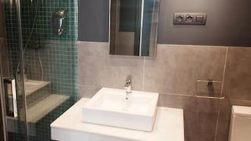 A modern bathroom with a glass shower enclosure, a white sink, and a mirror above it.