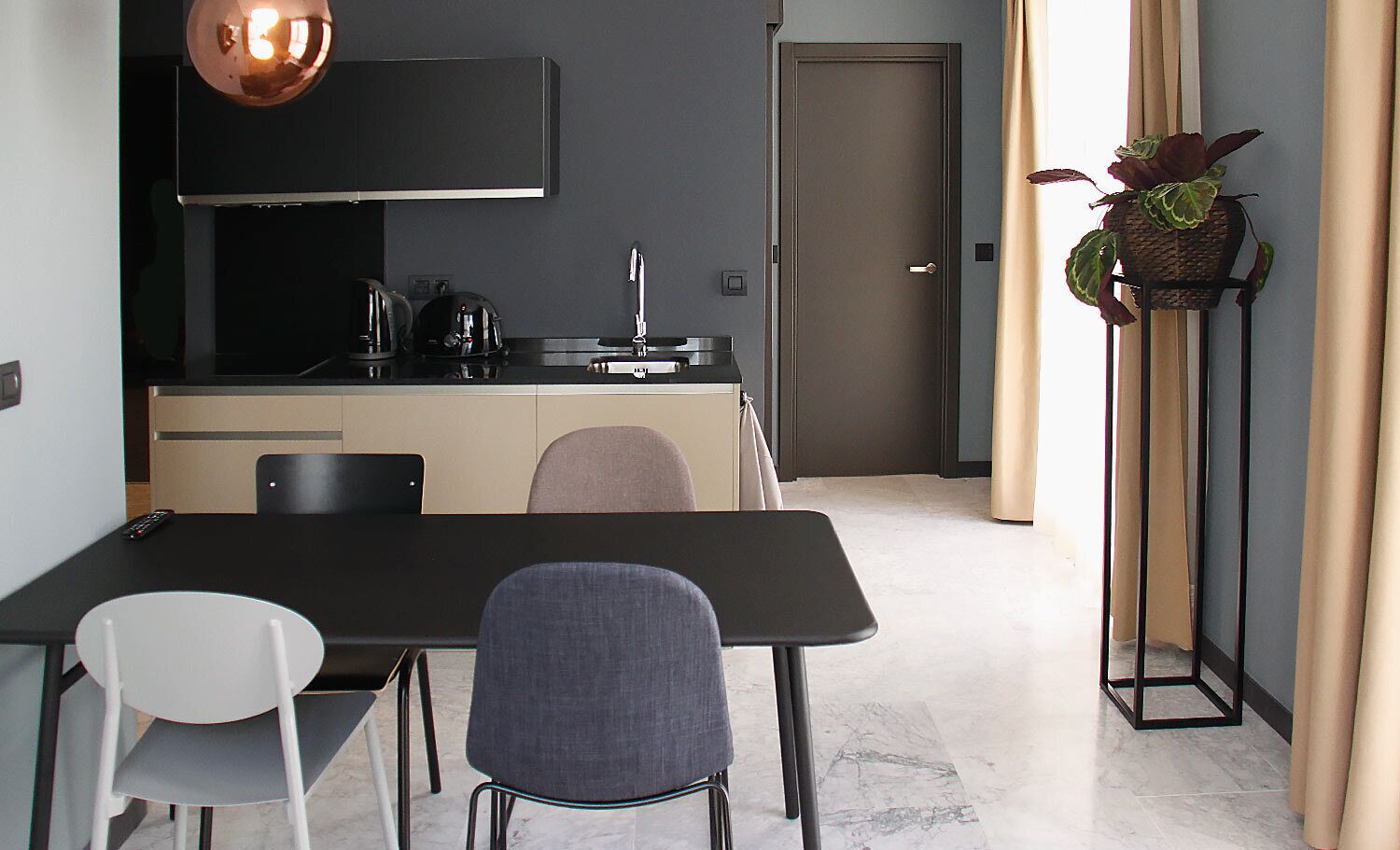 Een moderne keuken met een zwart aanrecht, een koperen hanglamp en een deur die naar een andere kamer leidt.