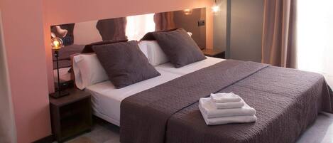 A neatly made bed with a brown blanket and pillows, a bedside lamp, and a folded towel on the nightstand.