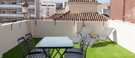 A rooftop terrace with a table and chairs, artificial grass, and a view of buildings.