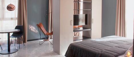 Una habitación de hotel moderna con cama, escritorio, silla, armario y televisor.