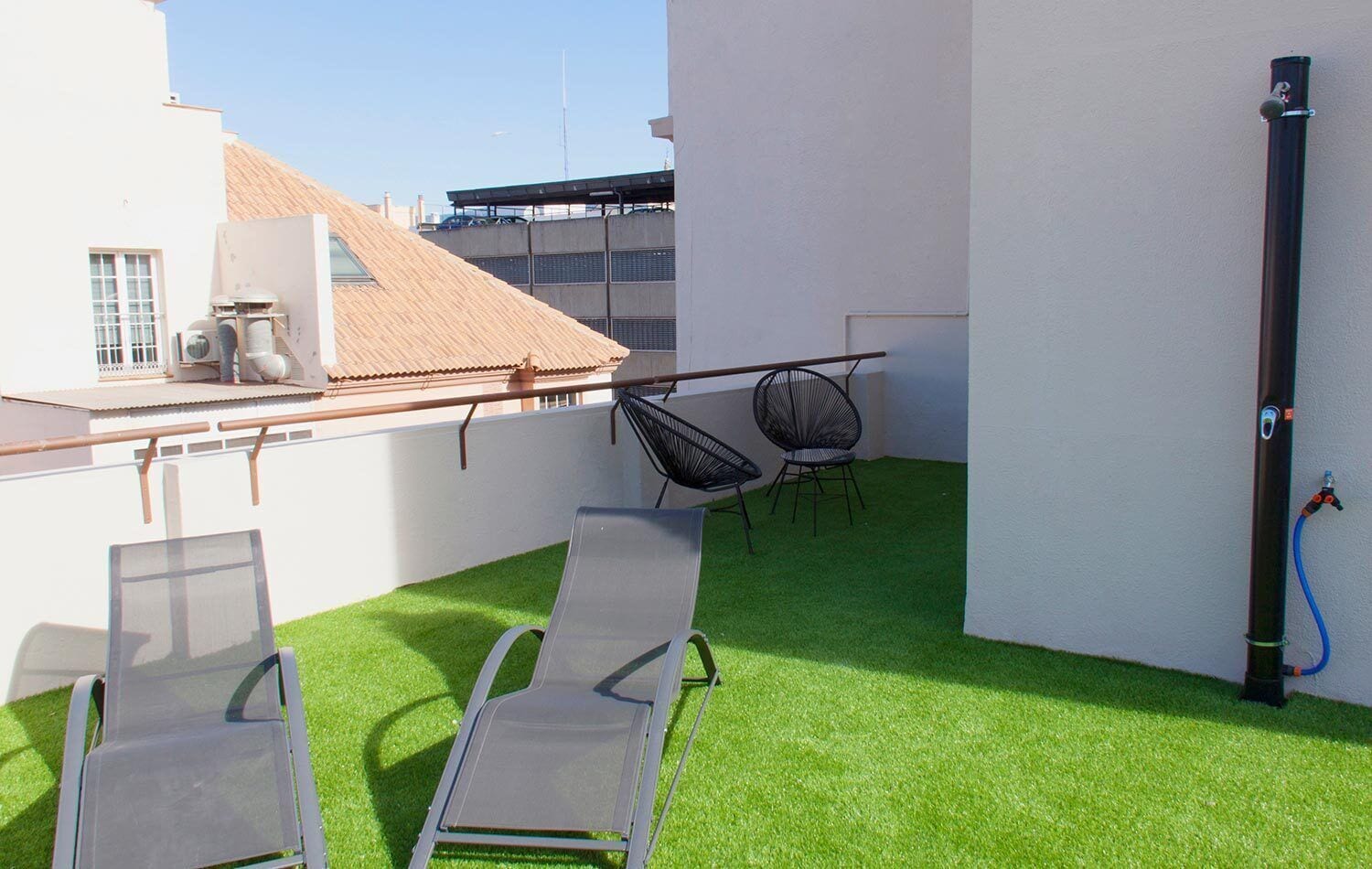 Eine Dachterrasse mit Kunstgras, zwei Liegestühlen, einem kleinen Tisch und einer Wasserpfeife.