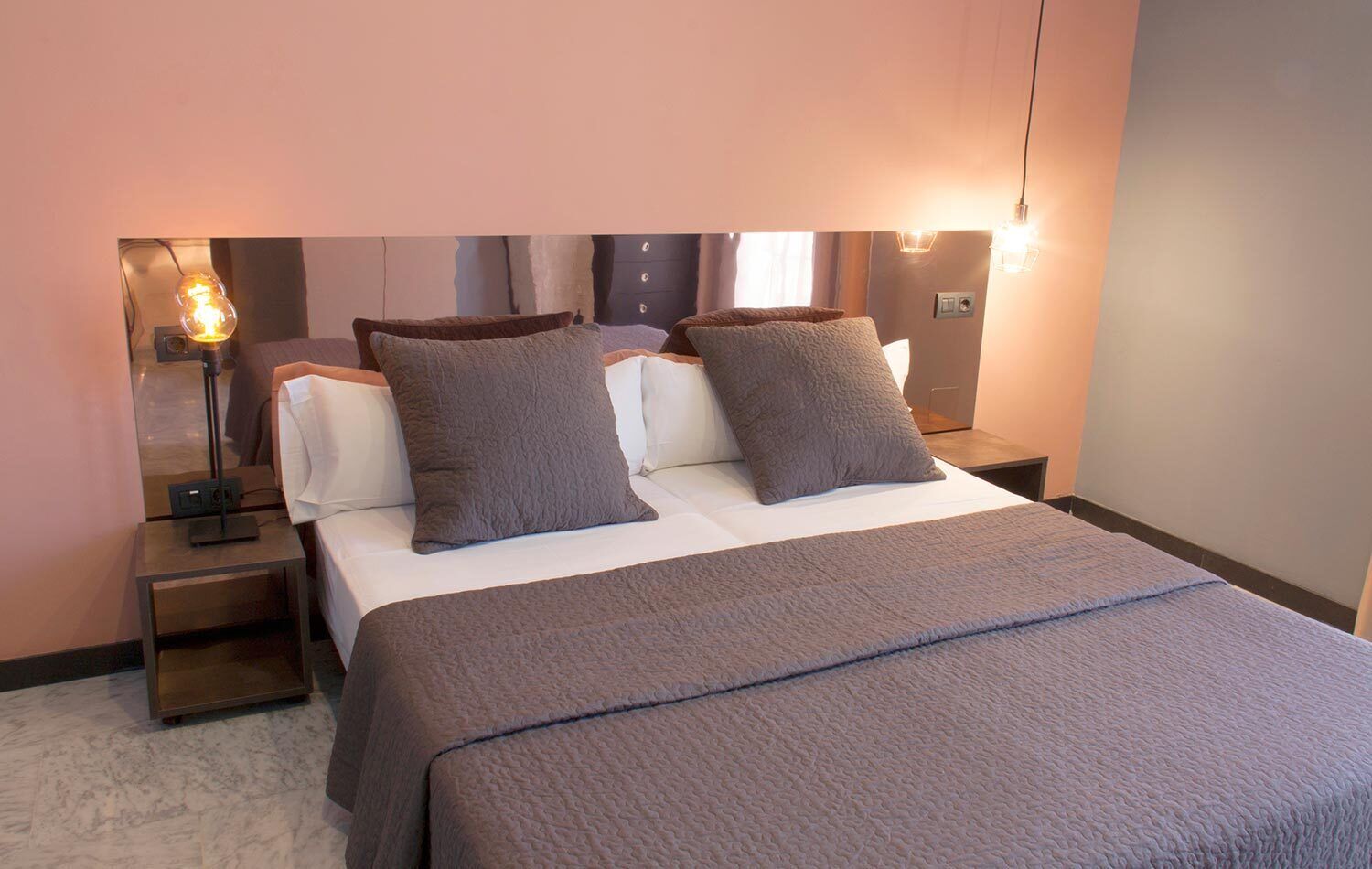 A hotel room with a bed, two bedside tables, a lamp, and a wall-mounted light fixture.