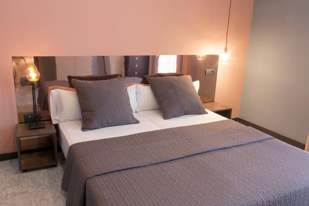 A hotel room with a bed, two bedside tables, a lamp, and a wall-mounted light fixture.