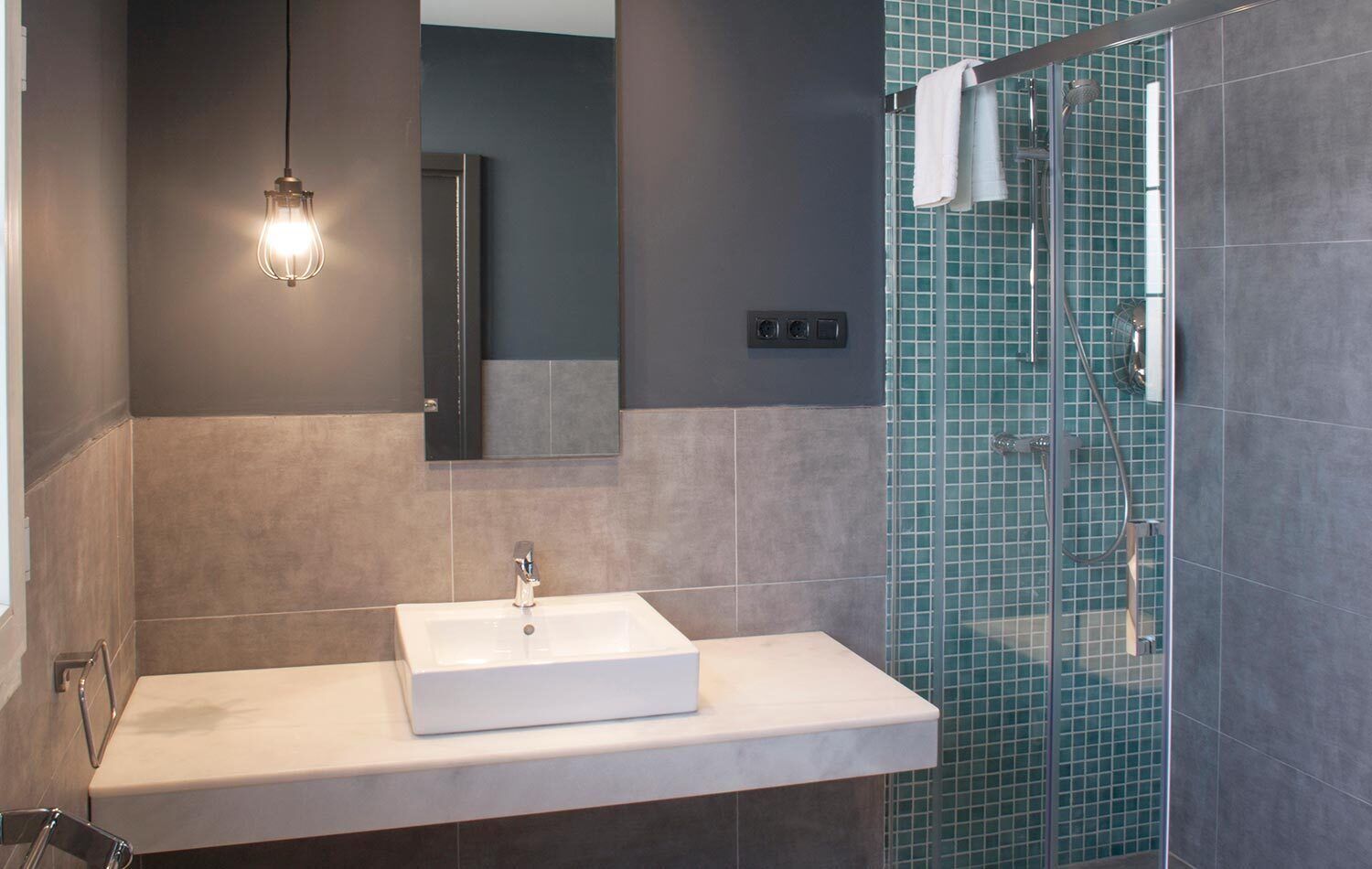 Ein modernes Badezimmer mit einem rechteckigen Waschbecken, einer Duschkabine aus Glas und einer Pendelleuchte.