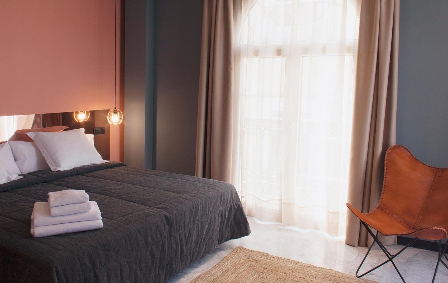 Een moderne hotelkamer met een groot bed, een stoel en een raam met dunne gordijnen.