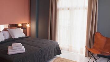 Een moderne hotelkamer met een groot bed, een stoel en een raam met dunne gordijnen.