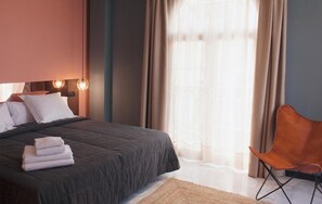 Una habitación de hotel moderna con una cama grande, una silla y una ventana con cortinas translúcidas.