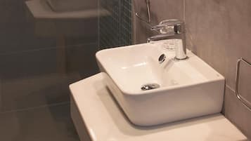 Un baño moderno con lavamanos blanco, grifo cromado y cabina de ducha de vidrio.