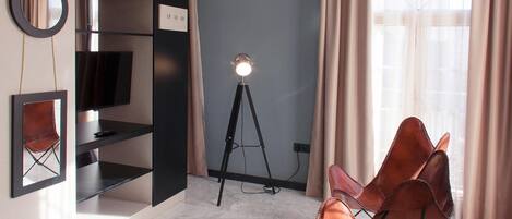 Una habitación moderna con una estantería negra, televisor montado, lámpara trípode y una silla de cuero.